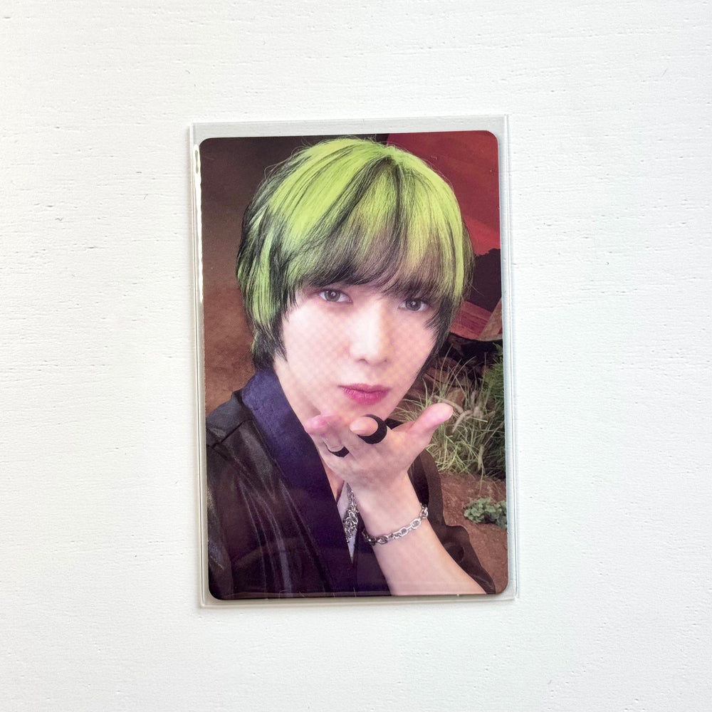 Portrait photocard with person holding hands near face, neon green hair and dark outfit
