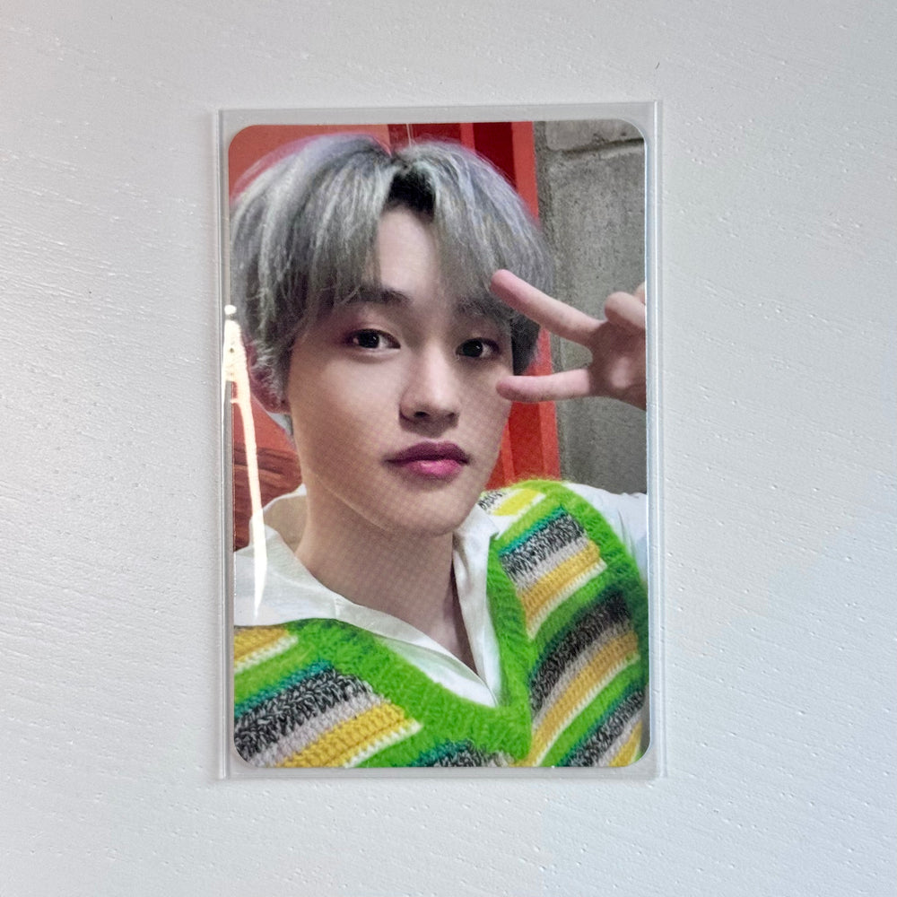 Photocard of young man with silver hair, green-yellow striped sweater, peace sign