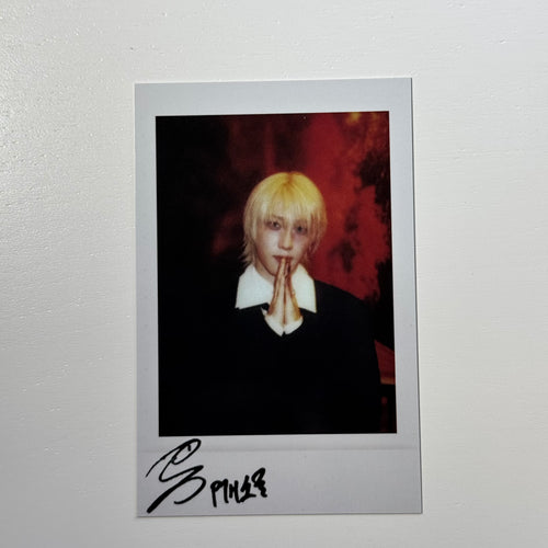 Signed polaroid photo card of a blond person in a dark top, hands clasped near face