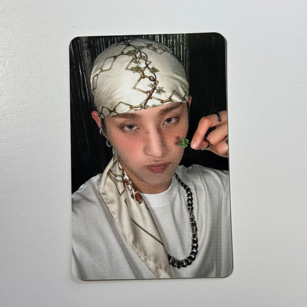 Portrait photocard of a man with patterned headscarf, white shirt, and chain necklace