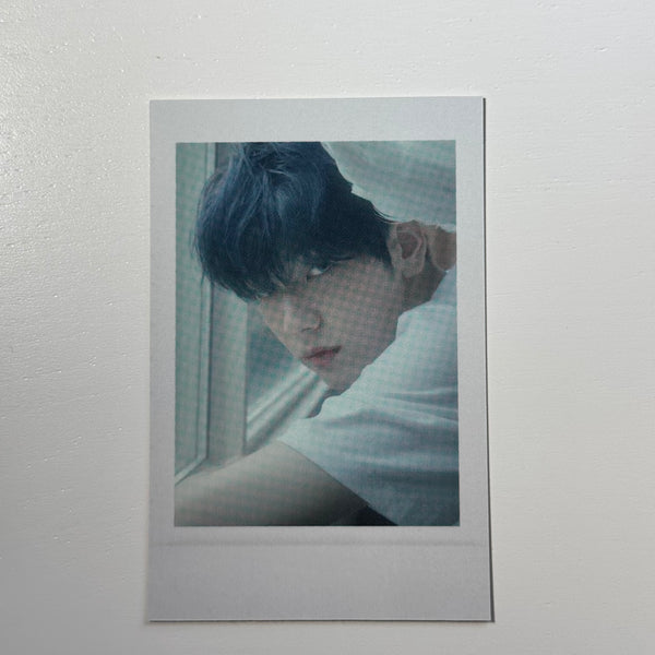 Polaroid photo of a person with dark hair, head bowed, in a light sweater
