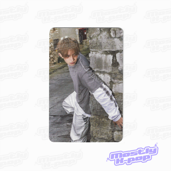 Rectangular photo card featuring a person in a gray top and white pants, standing outdoors.