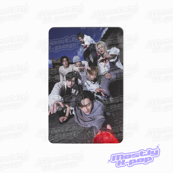 Rectangular photo card showing a group of people outdoors posing together, wearing light outfits.